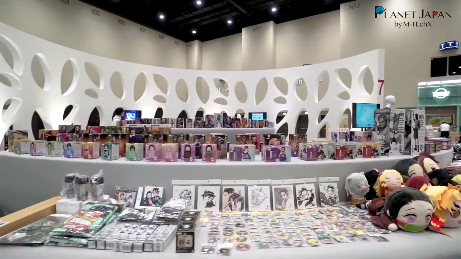 A curved white display wall of cut-out panels filled with products at an exhibition pavilion