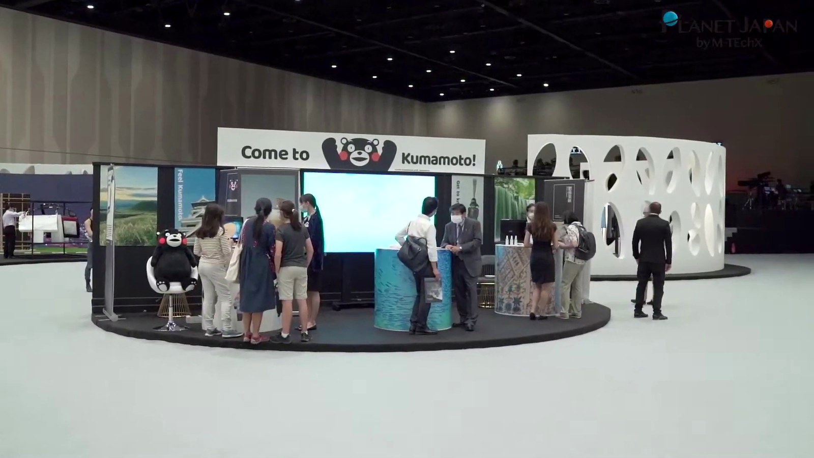 Exhibition floor with a screen, island stand and visitors in a large hall