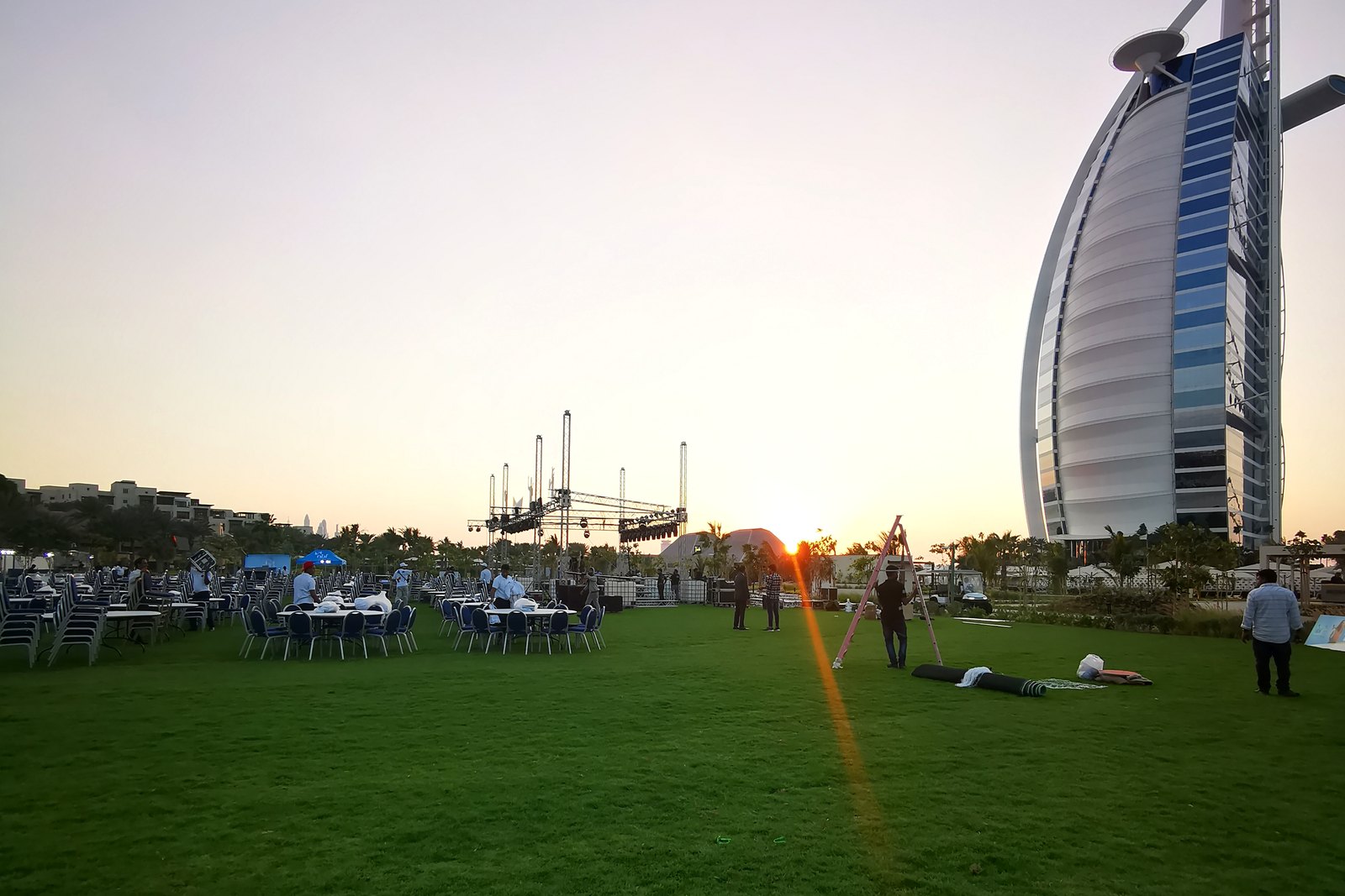 An event lawn at sunset with the Burj Al Arab behind, tables and truss being set