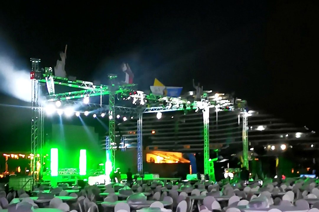 The stage lit green at night with seated tables in front