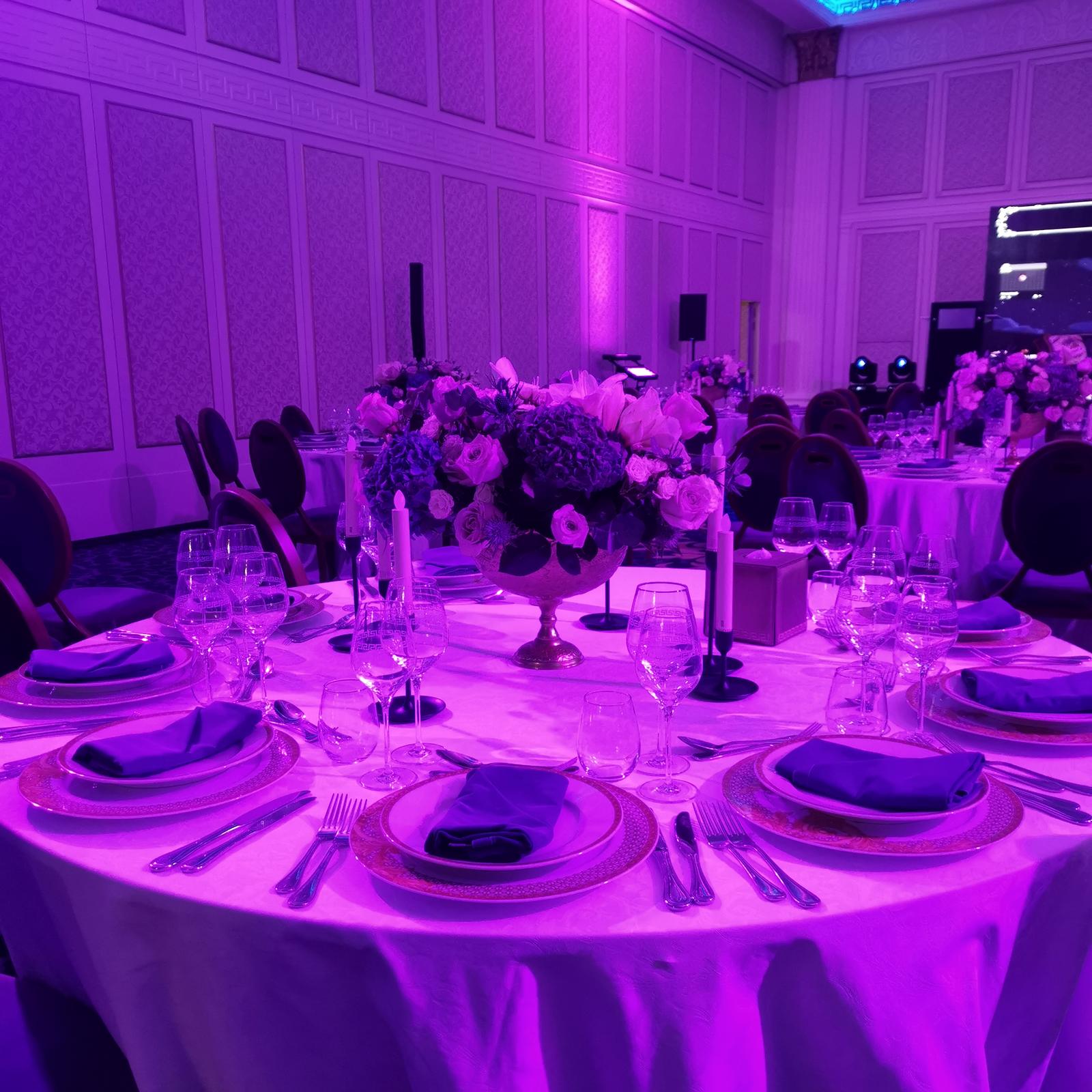 Place settings and glassware on a round table under magenta light